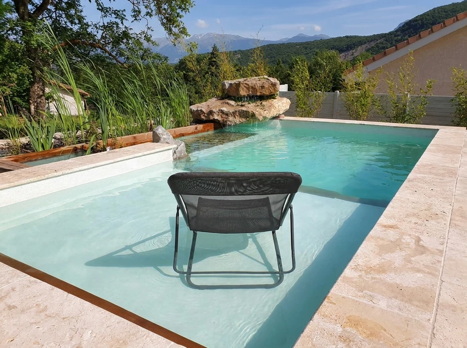 Piscine extérieure à débordement partiel avec plage immergée en travertin