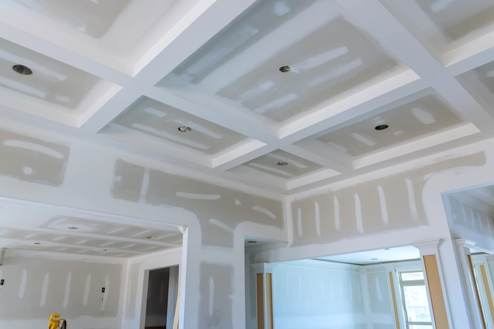 Intérieur de maison en construction avec plafond à caissons géométriques et cloisons en cours de finition