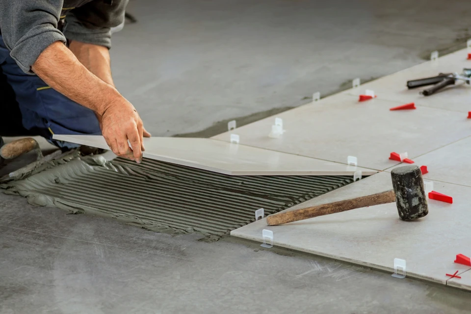 Artisan carreleur installant du carrelage sur chape ciment en intérieur