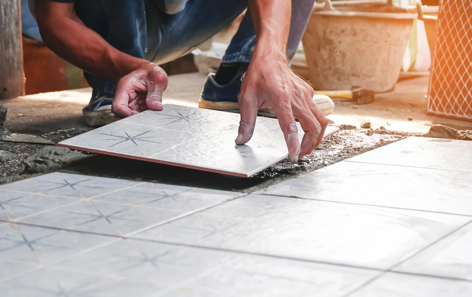Ouvrier en position accroupie installant un carrelage en céramique sur une surface préparée, utilisant ses mains pour positionner précisément une dalle décorative à motifs géométriques