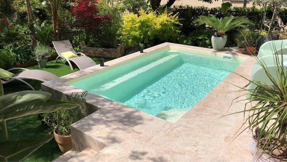 Piscine à débordement rectangulaire de type lap pool, entourée d'un dallage en travertin beige