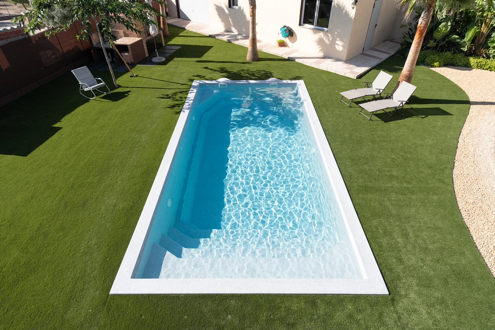 Piscine à débordement rectangulaire de type lap pool, entourée d'un dallage en travertin beige